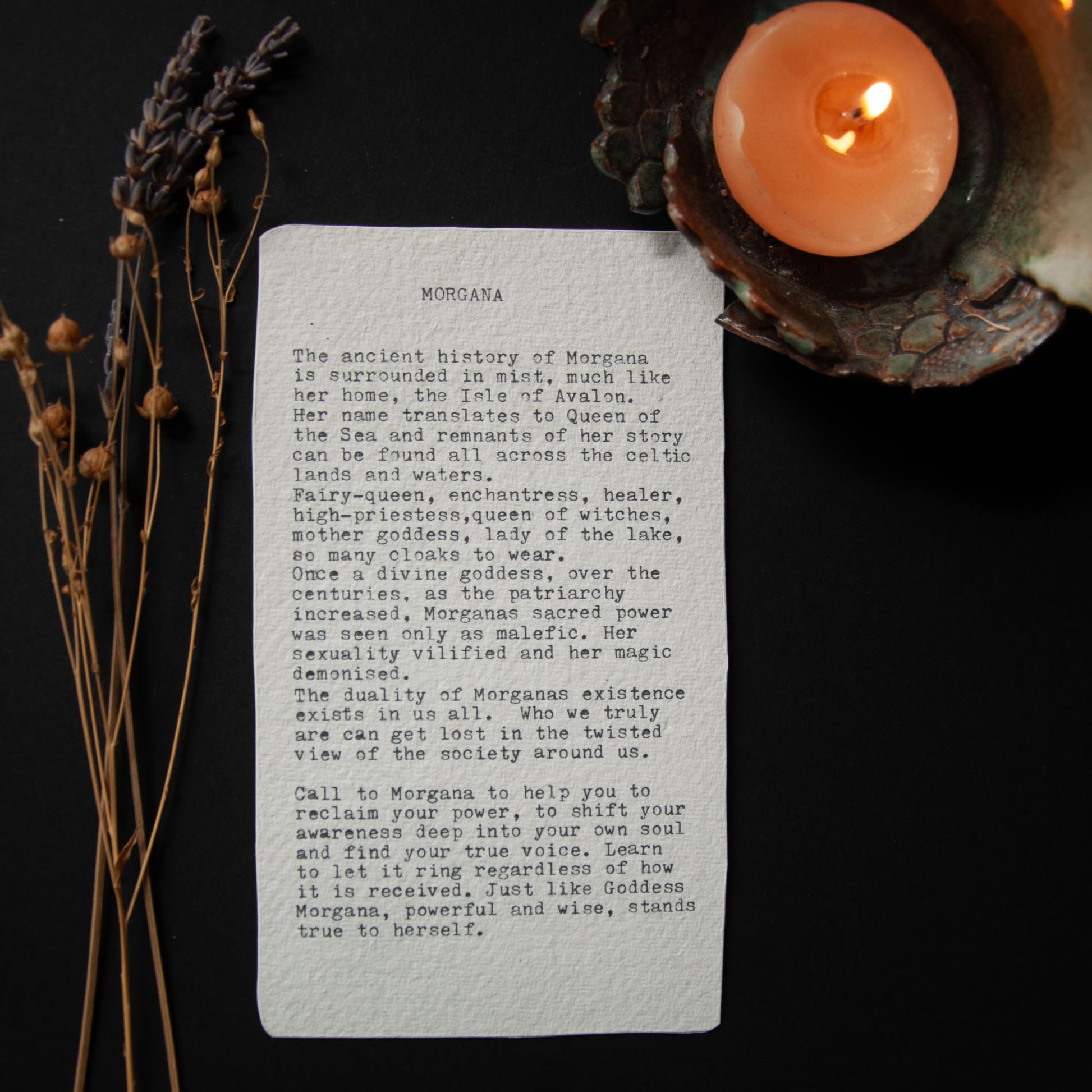 Sheet of paper with text, candle, and dried plants on a dark background