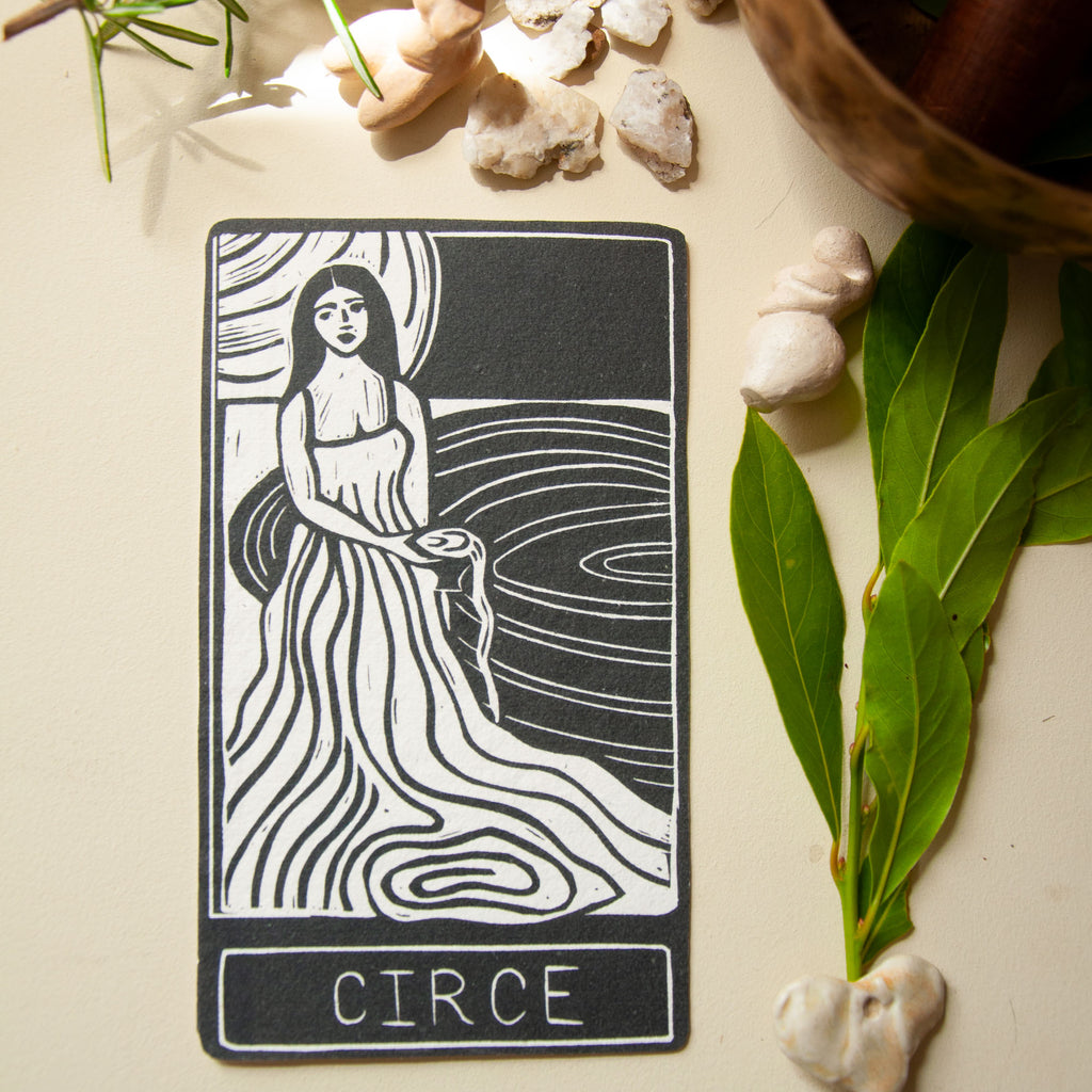 Tarot card featuring a woman labeled 'Circe' on a surface with leaves and stones.