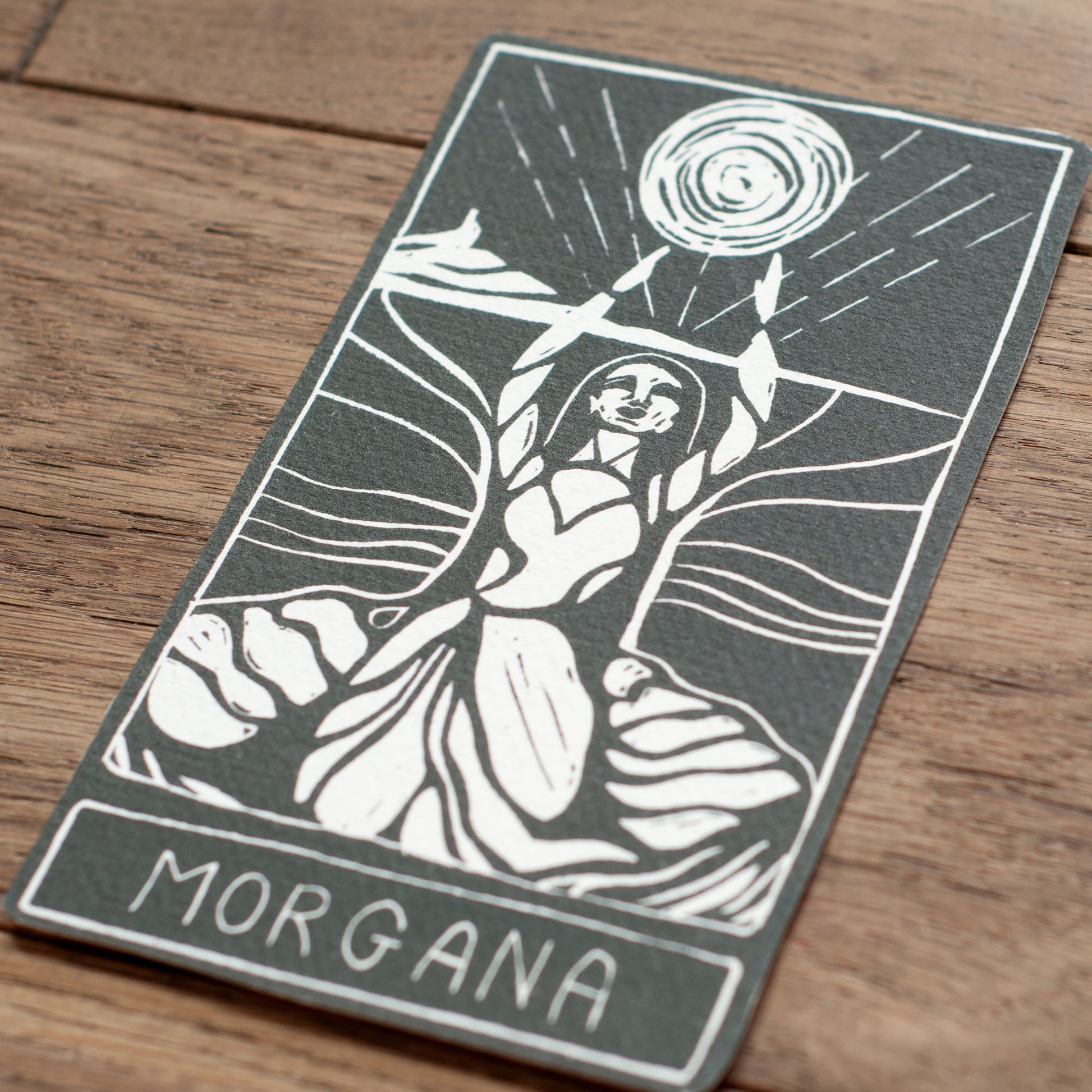 Tarot card featuring a stylized illustration of a figure with 'Morgana' at the bottom, on a wooden surface.