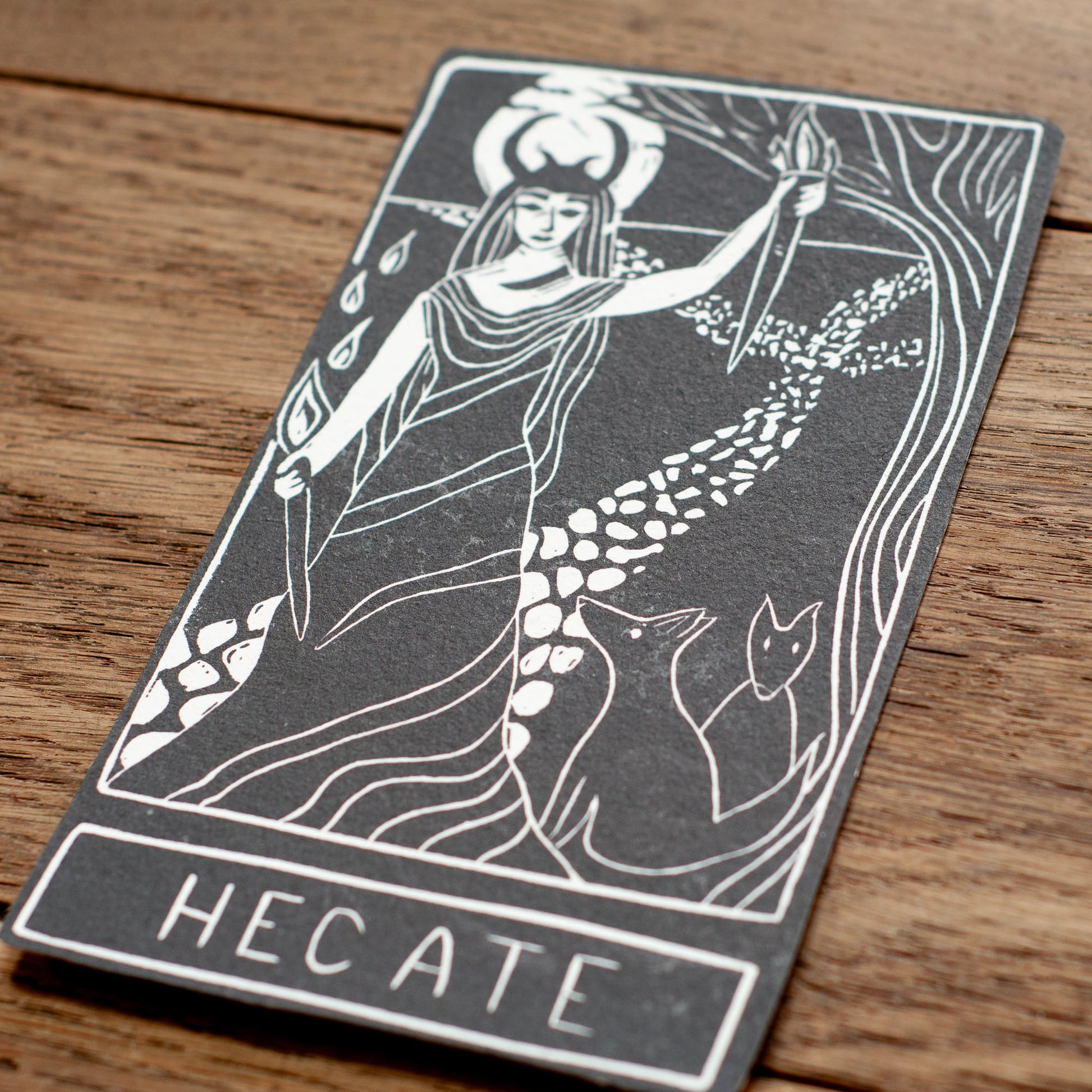 Card featuring the depiction of Hecate with a sword and torch on a wooden surface
