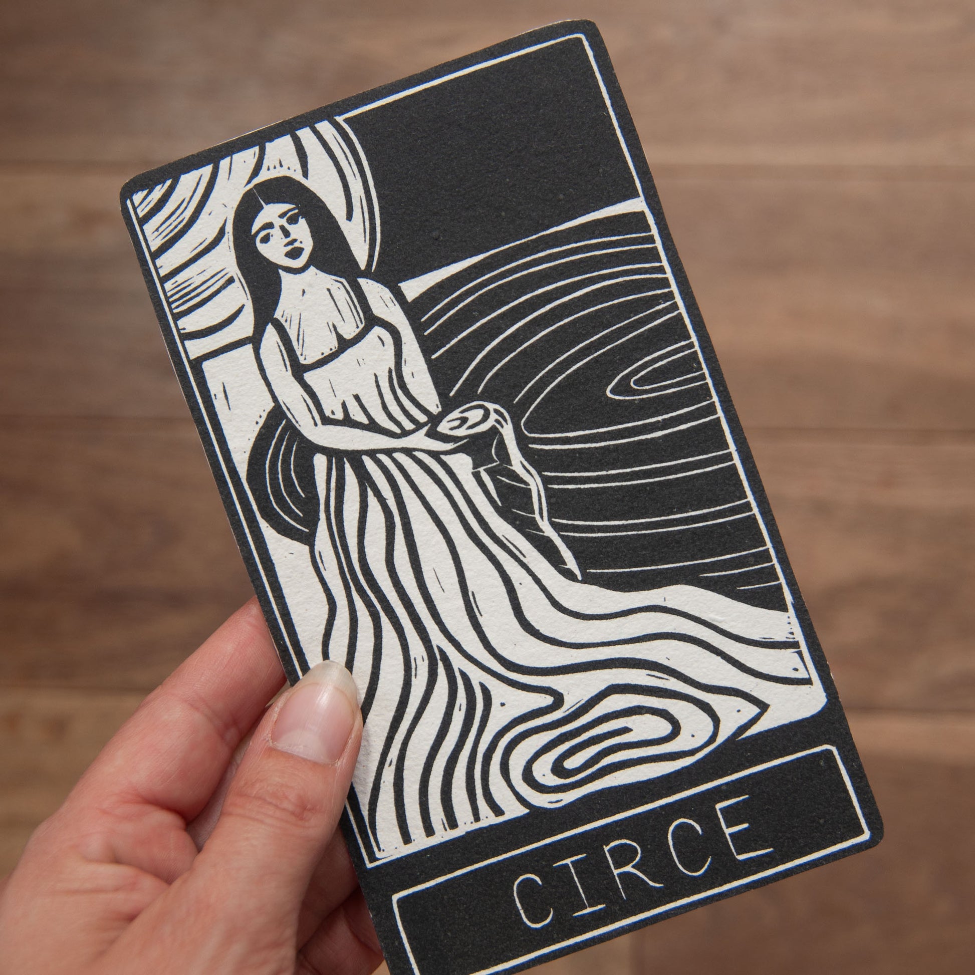 Tarot card featuring a woman labeled 'Circe' held by a hand on a wooden surface