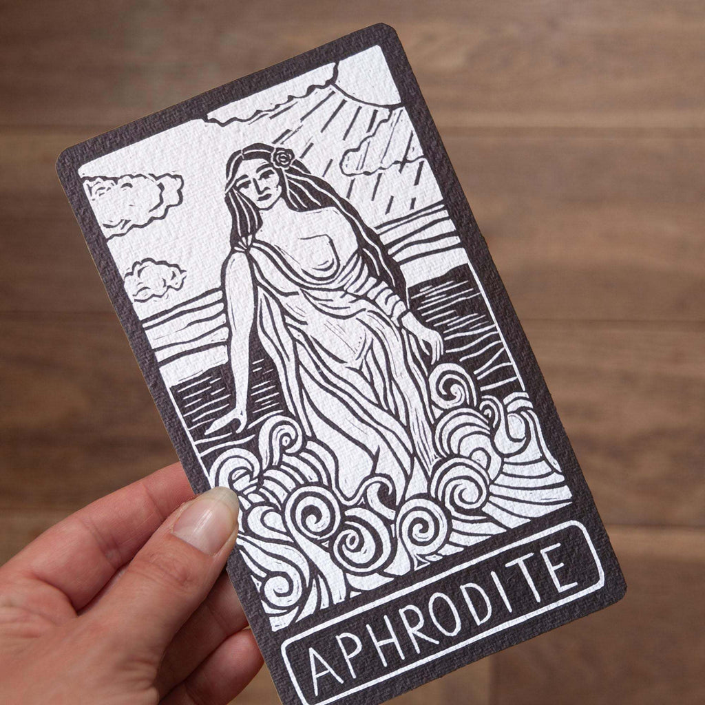 APHRODITE ALTAR CARD with black linocut-style goddess illustration on off-white textured card, framed by a dark border