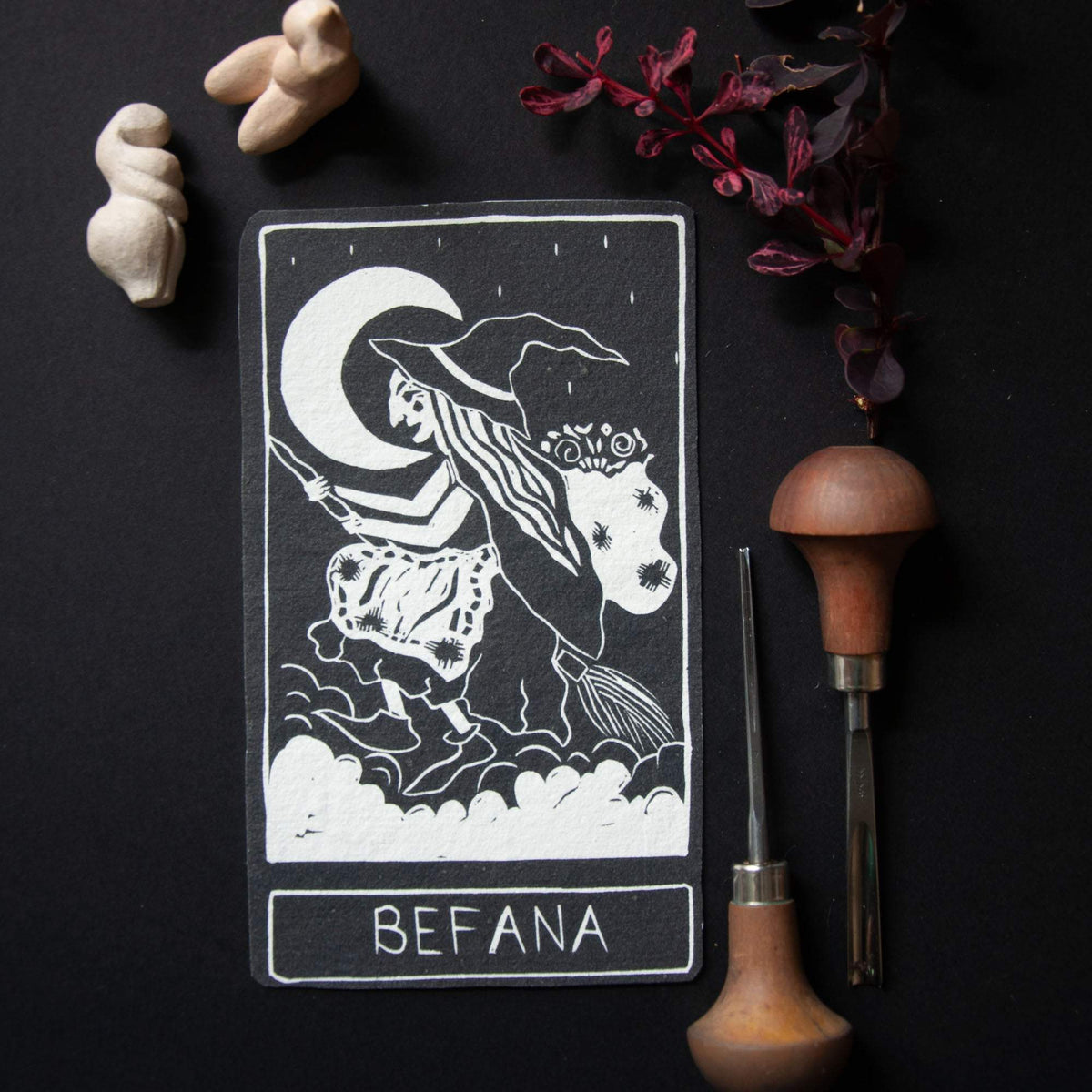 BEFANA ORACLE CARD featuring a monochrome black-and-white linocut witch flying across a crescent moon, with a white border and lettering.