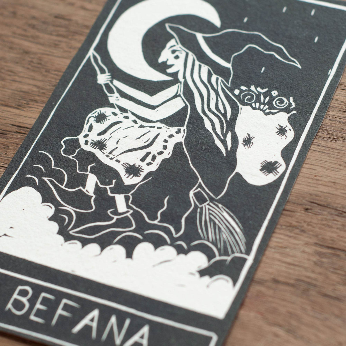 BEFANA ORACLE CARD featuring a black-and-white linocut of a witch riding a broom beneath a crescent moon.