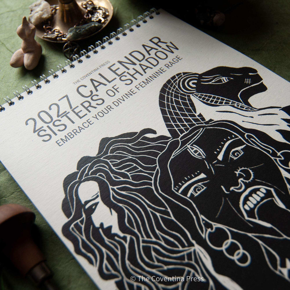 Dark Goddess Calendar 2027 with a black-and-white linocut cover showing intertwined goddess faces and spiral binding