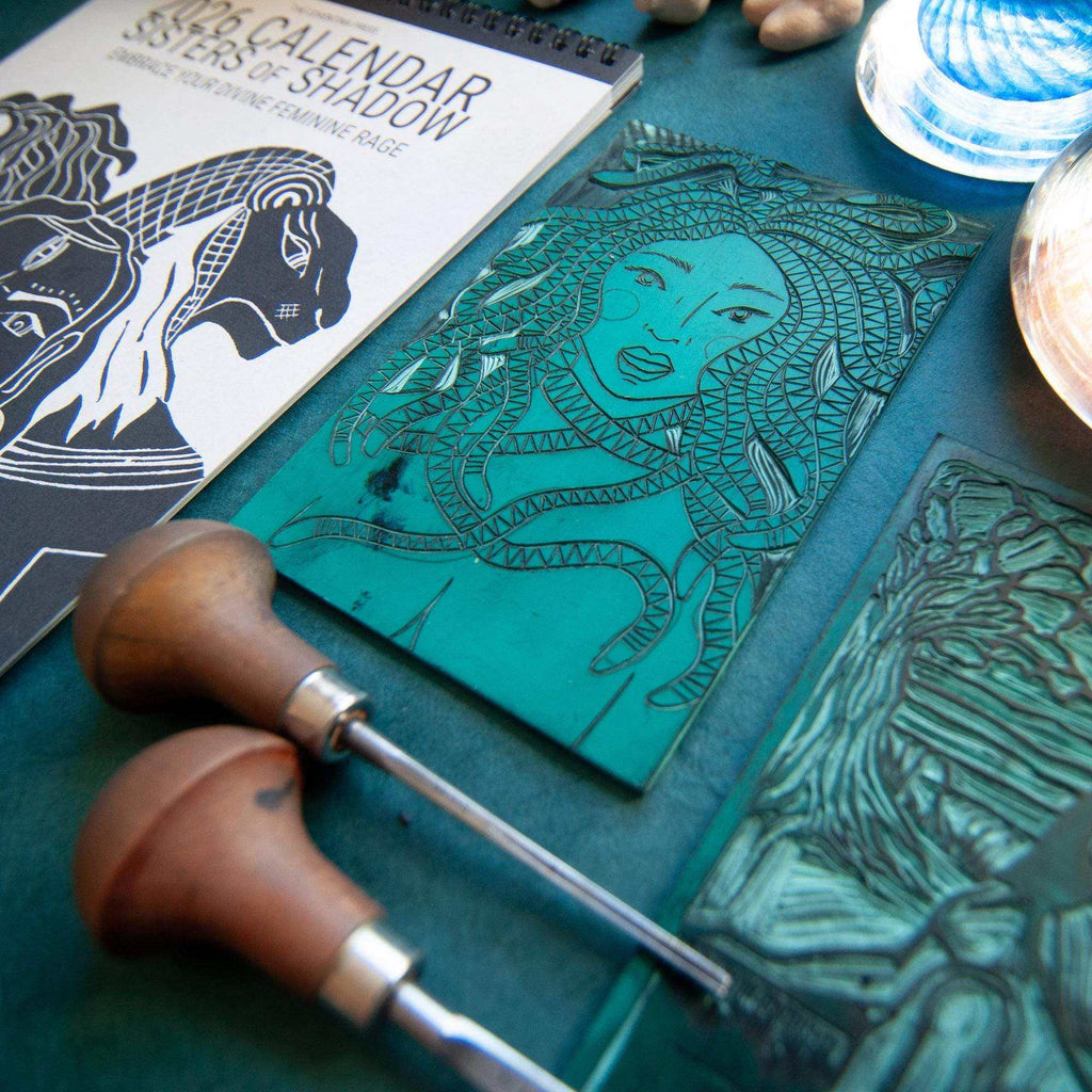 Dark Goddess Calendar 2027 with a black-and-white goddess linocut cover beside turquoise carved printing blocks and tools
