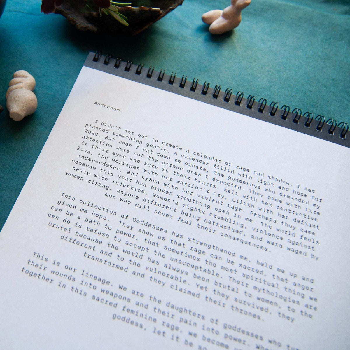 Dark Goddess Calendar 2027 with a white spiral-bound page of printed text and black binding