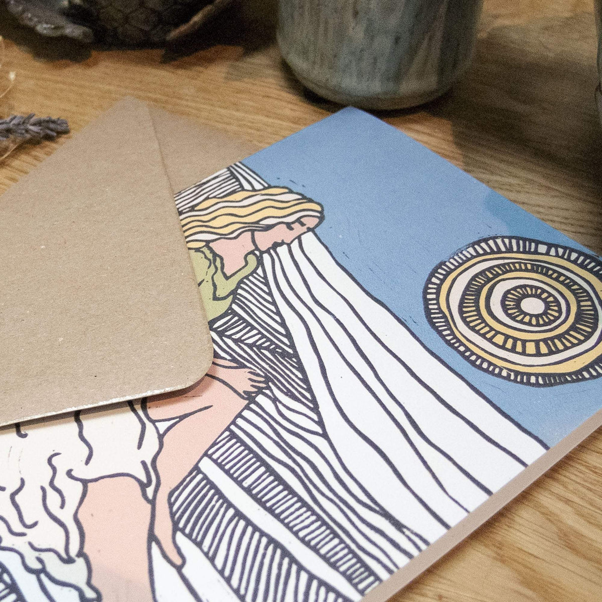 DEMETER Greeting card with a blue background, featuring a woman in a striped white robe and a circular sun motif in linocut style.