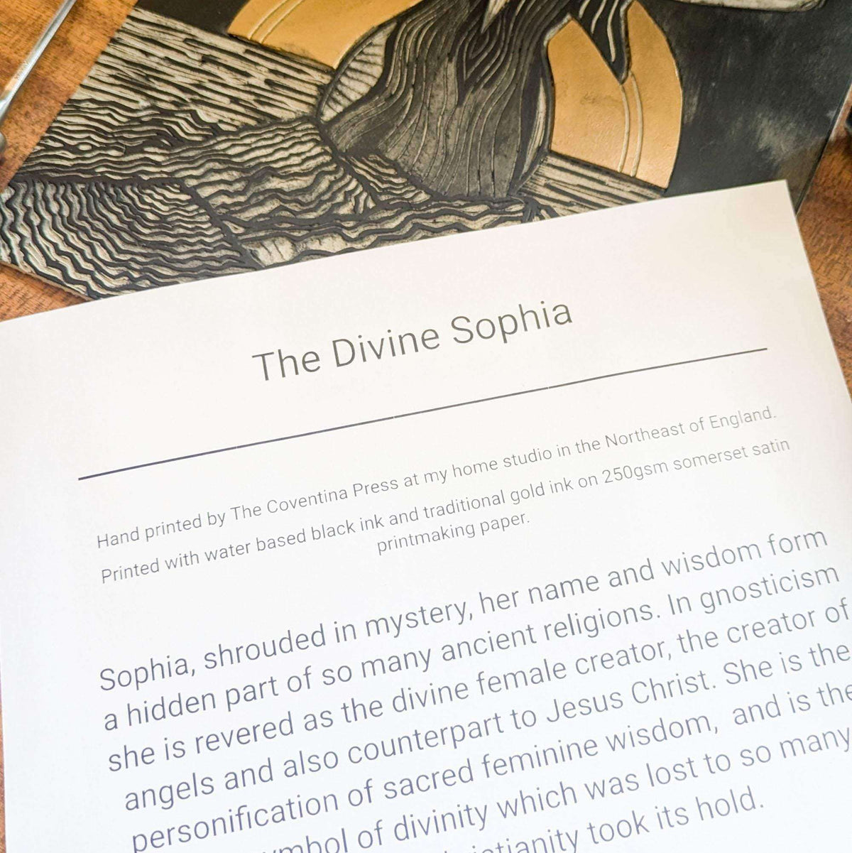 Divine Sophia Art linocut print with black carved lines, gold-toned shapes and text on white paper