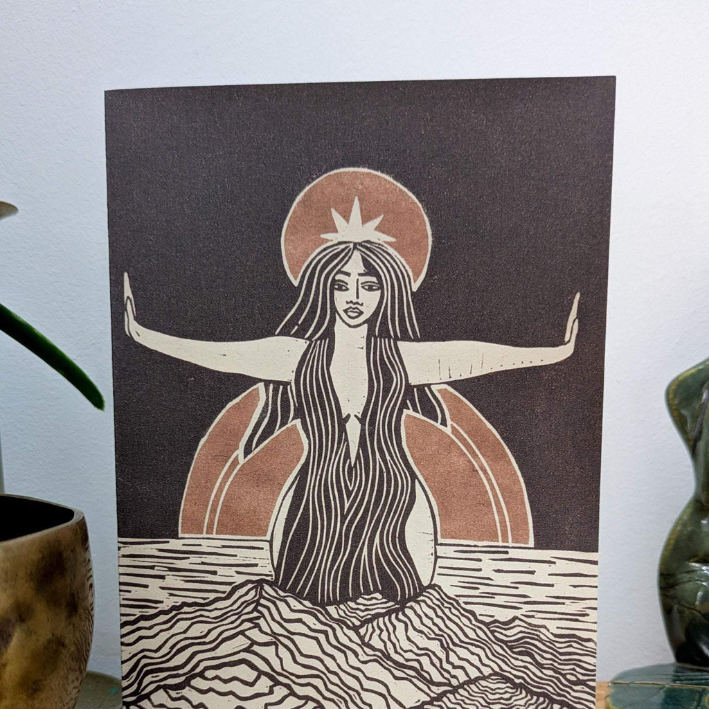 Divine Sophia Greeting card featuring a woman with flowing hair, raised arms and a rust-coloured halo in a black linocut design