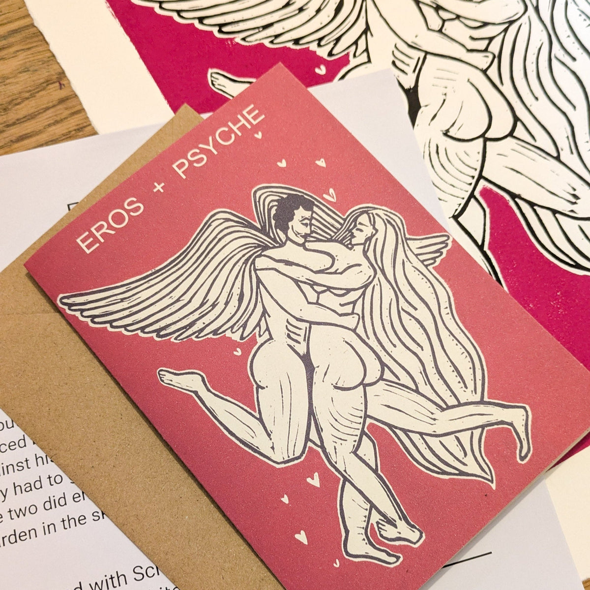 EROS AND PSYCHE Greeting card in muted red cardstock, with a cream-and-black linocut of embracing winged figures and hearts.