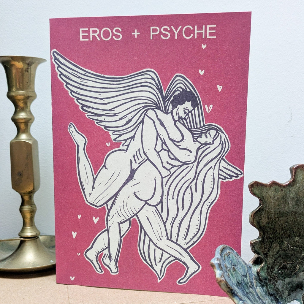 EROS AND PSYCHE Greeting card in raspberry pink with a white-and-black linocut of winged lovers and small hearts.