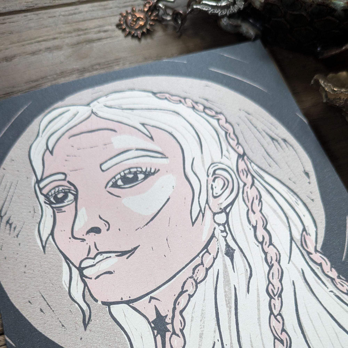 Frigg Greeting card in muted gray and blush, featuring a monochrome linocut portrait of a braided-haired goddess.