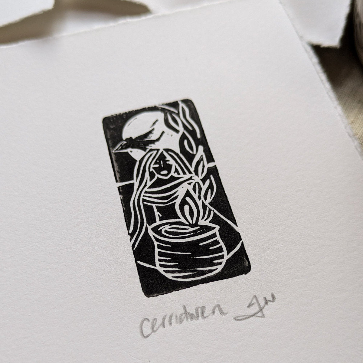 GODDESS CERRIDWEN miniature black linocut print on white paper, depicting a robed woman beside a cauldron