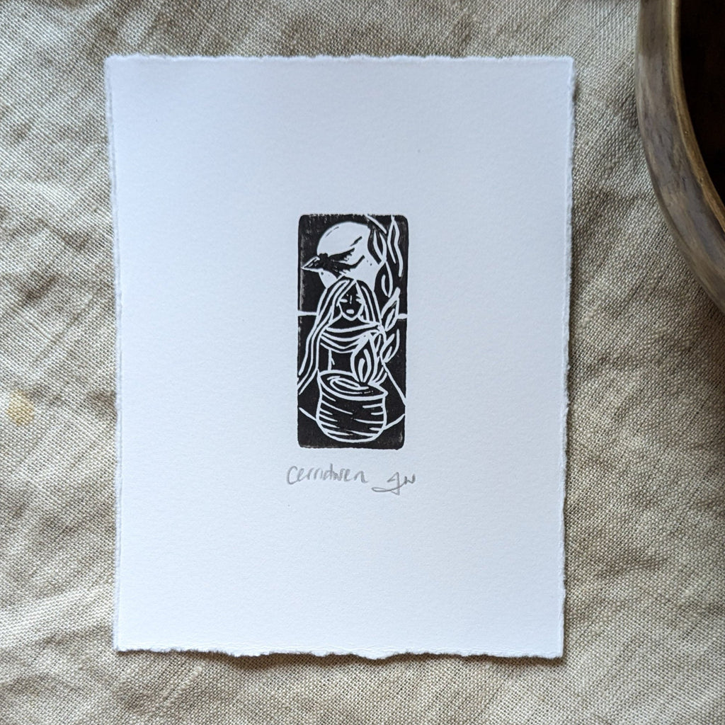 GODDESS CERRIDWEN miniature black linocut print on white paper, featuring a flowing-haired figure beside a cauldron
