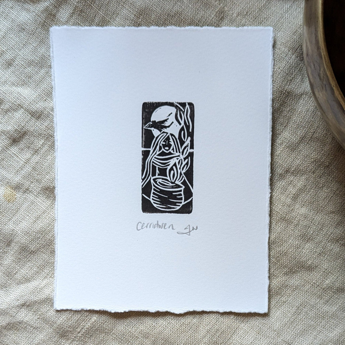 GODDESS CERRIDWEN miniature black linocut print on white paper, featuring a flowing-haired figure beside a cauldron