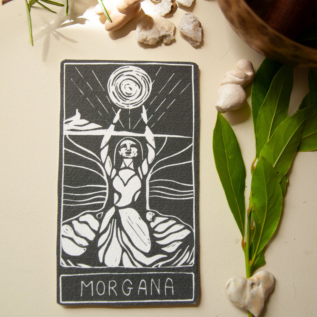 MORGANA ORACLE CARD in black and cream, featuring a handmade linocut of a robed goddess beneath a swirling sun