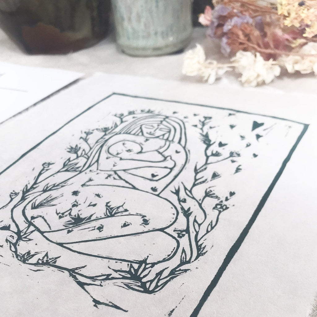 MOTHER AND BABE linocut print in dark green ink, depicting a mother cradling her baby among leaves and blossoms