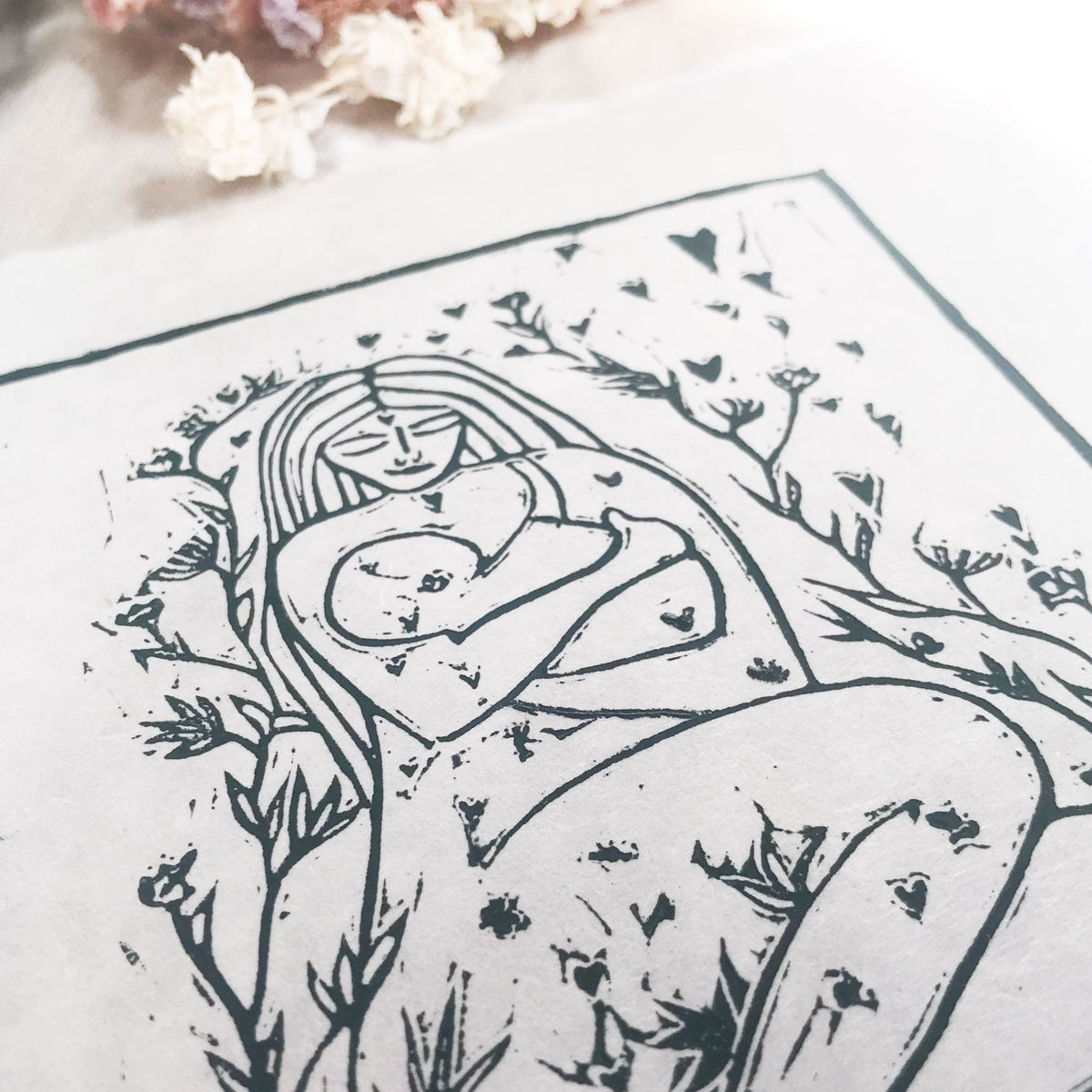 MOTHER AND BABE linocut print in dark green ink, showing a mother cradling her baby amid leafy branches