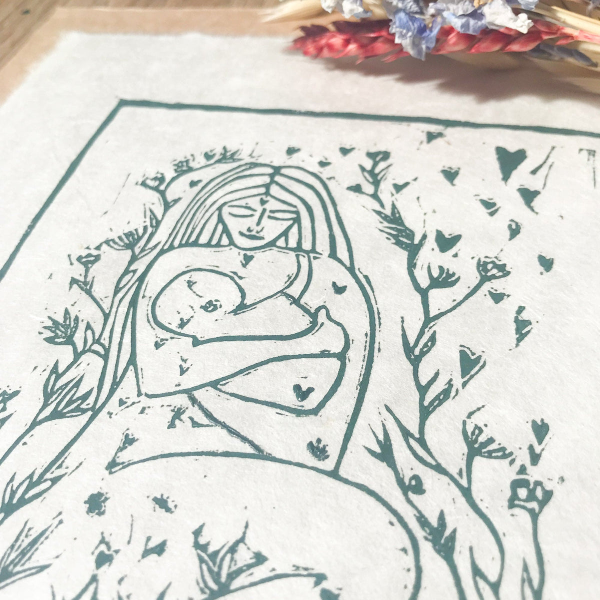 MOTHER AND BABE linocut print in dark green ink, showing a mother cradling her baby amid leafy branches