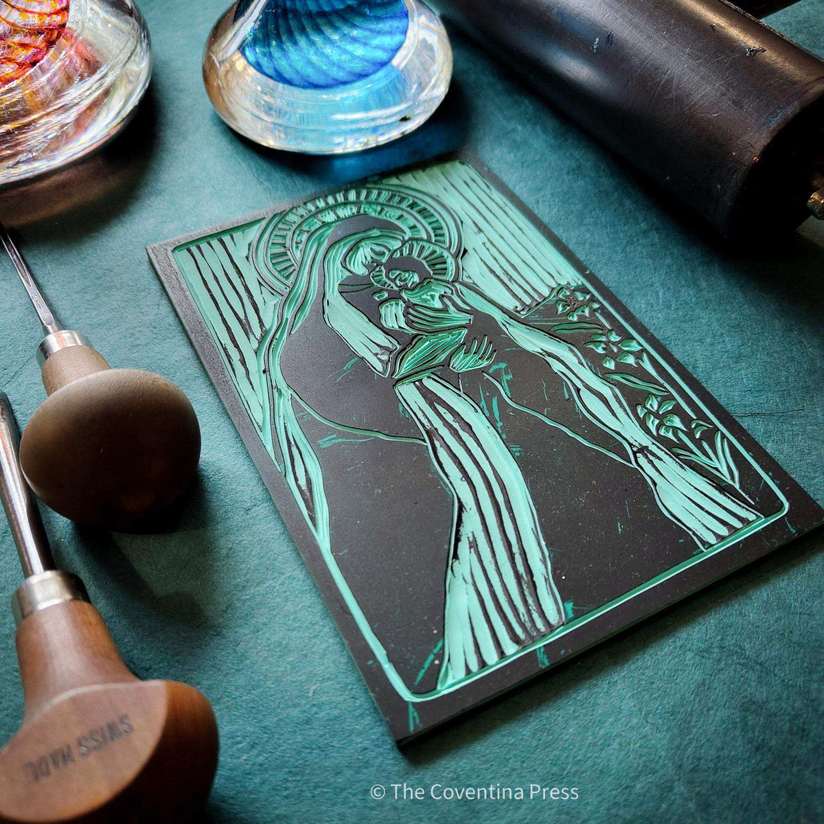 MOTHER MARY ALTAR CARD with a teal and black linocut-style image of Mary holding a child, framed by decorative lines