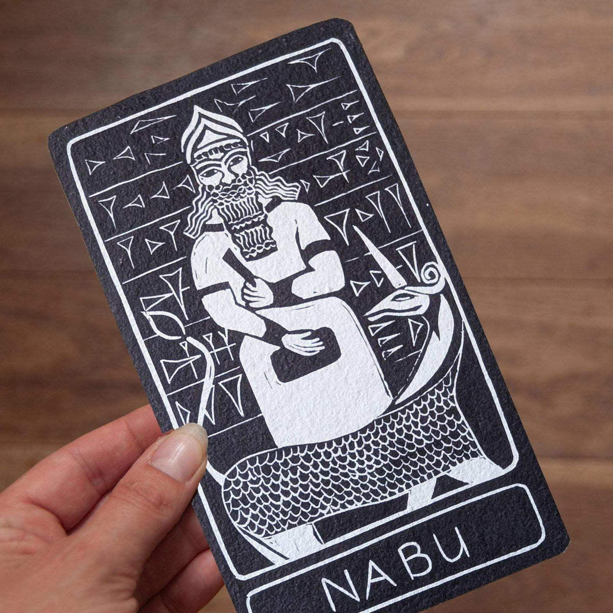 NABU ALTAR CARD with a black-and-white linocut-style figure, cuneiform-inspired marks, and a textured cotton rag surface