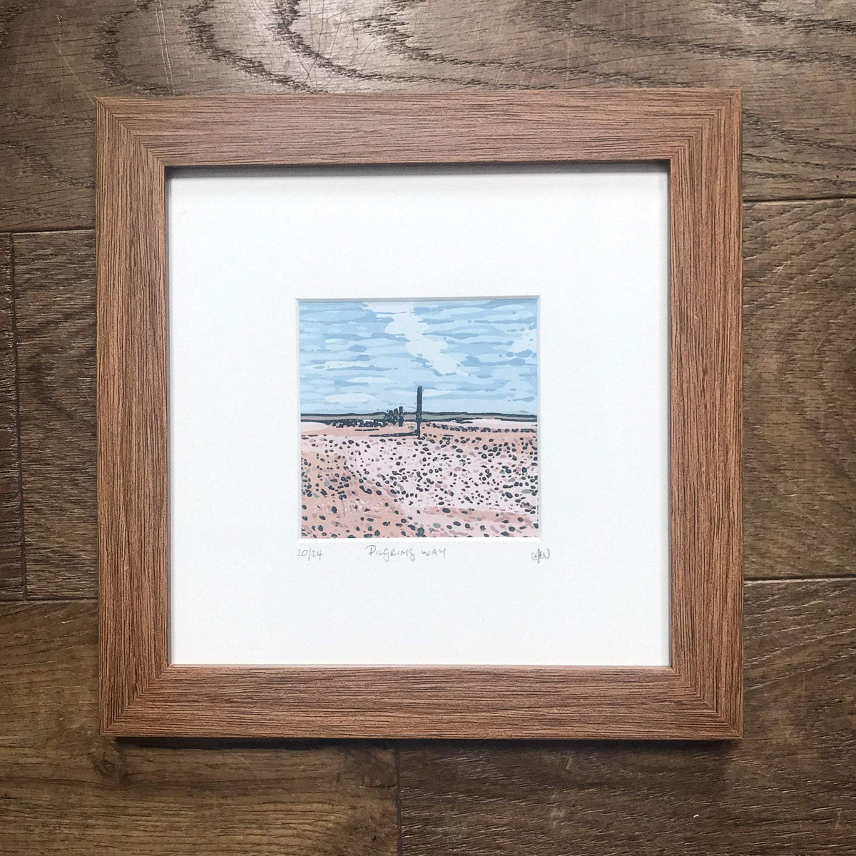 PILGRIM'S WAY linocut print showing a pale pink coastal path, blue sky and distant dark horizon, framed in wood