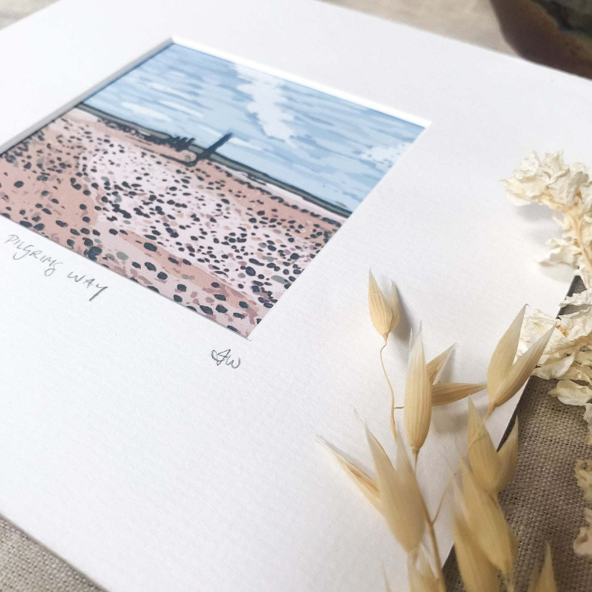 PILGRIM'S WAY linocut print with a blue sky, distant cross and pink pebble-strewn path on cream paper
