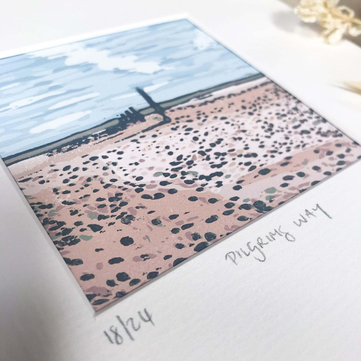 PILGRIM'S WAY linocut print showing a pink, dark-speckled shoreline beneath a pale blue sky and distant horizon
