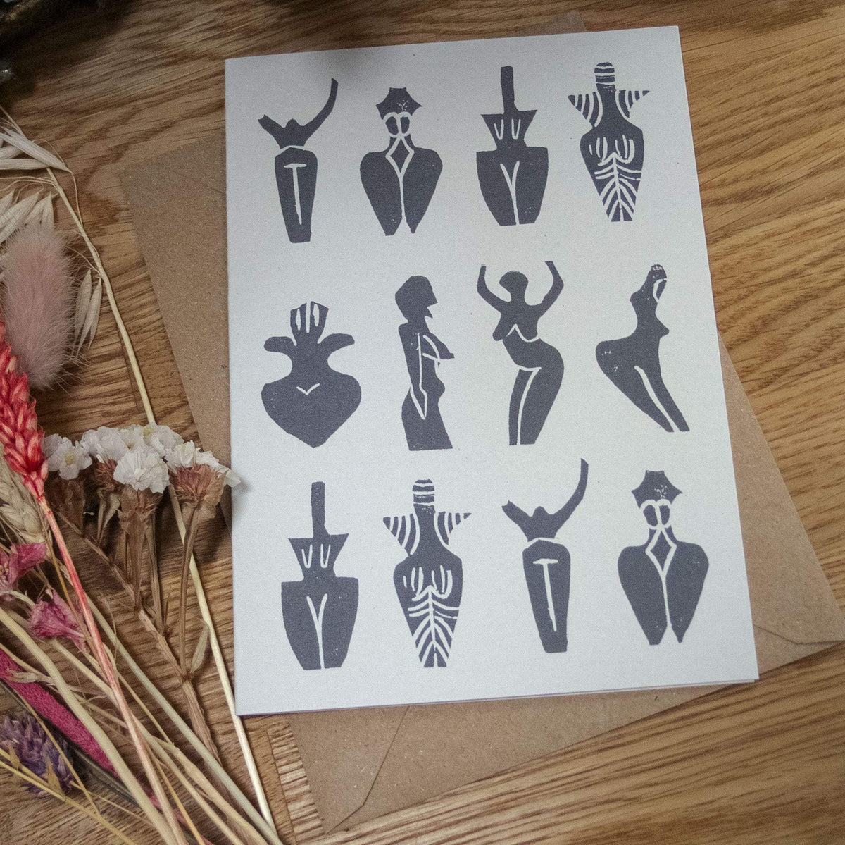 PREHISTORIC GODDESS GREETING CARD in natural white recycled cardstock, featuring a dark grey linocut pattern of stylized goddess figures.