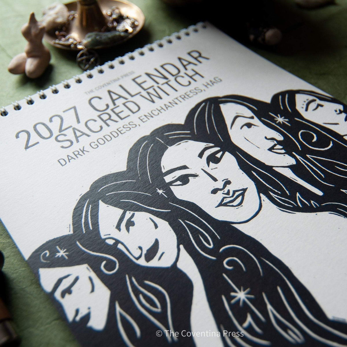 SACRED WITCH 2027 calendar with black-and-white linocut art of goddess faces on a natural paper cover