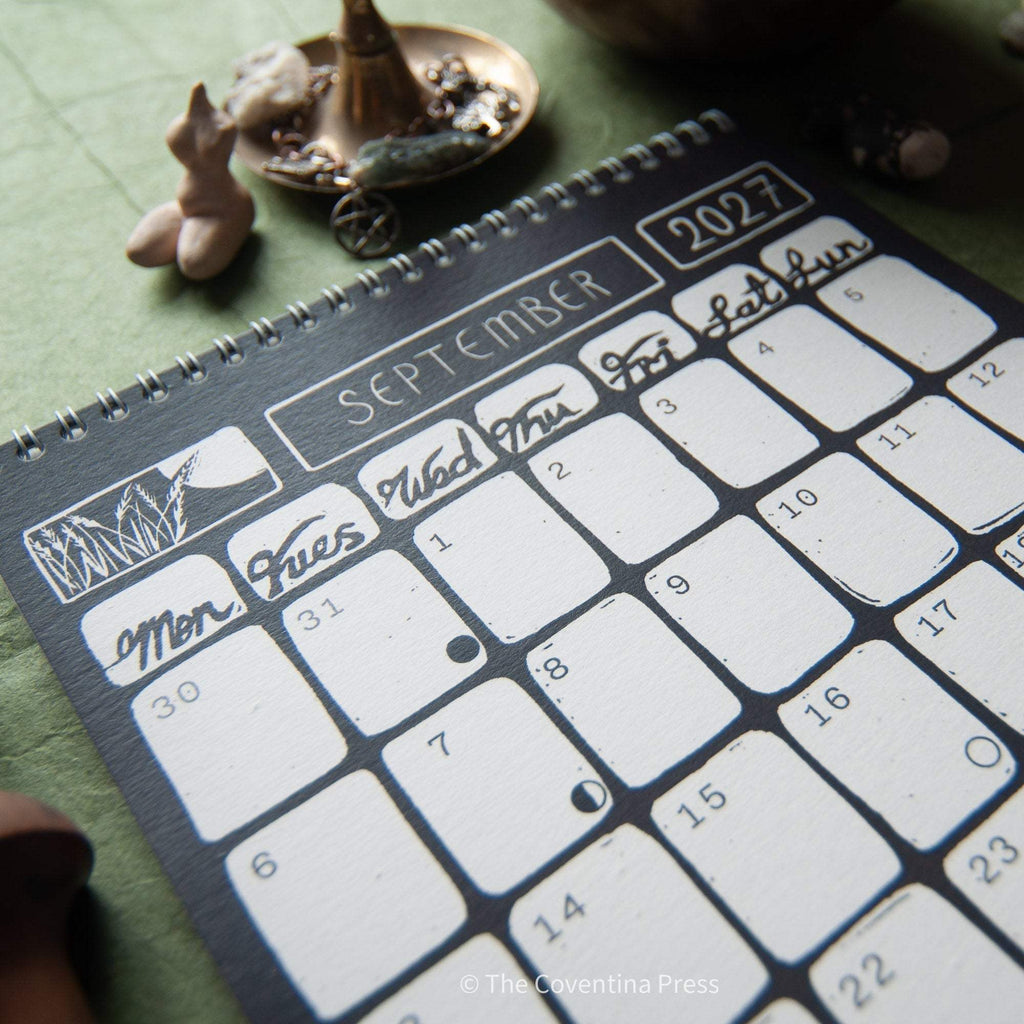 SACRED WITCH 2027 calendar with black and white September monthly grid, moon phases, and metal spiral binding