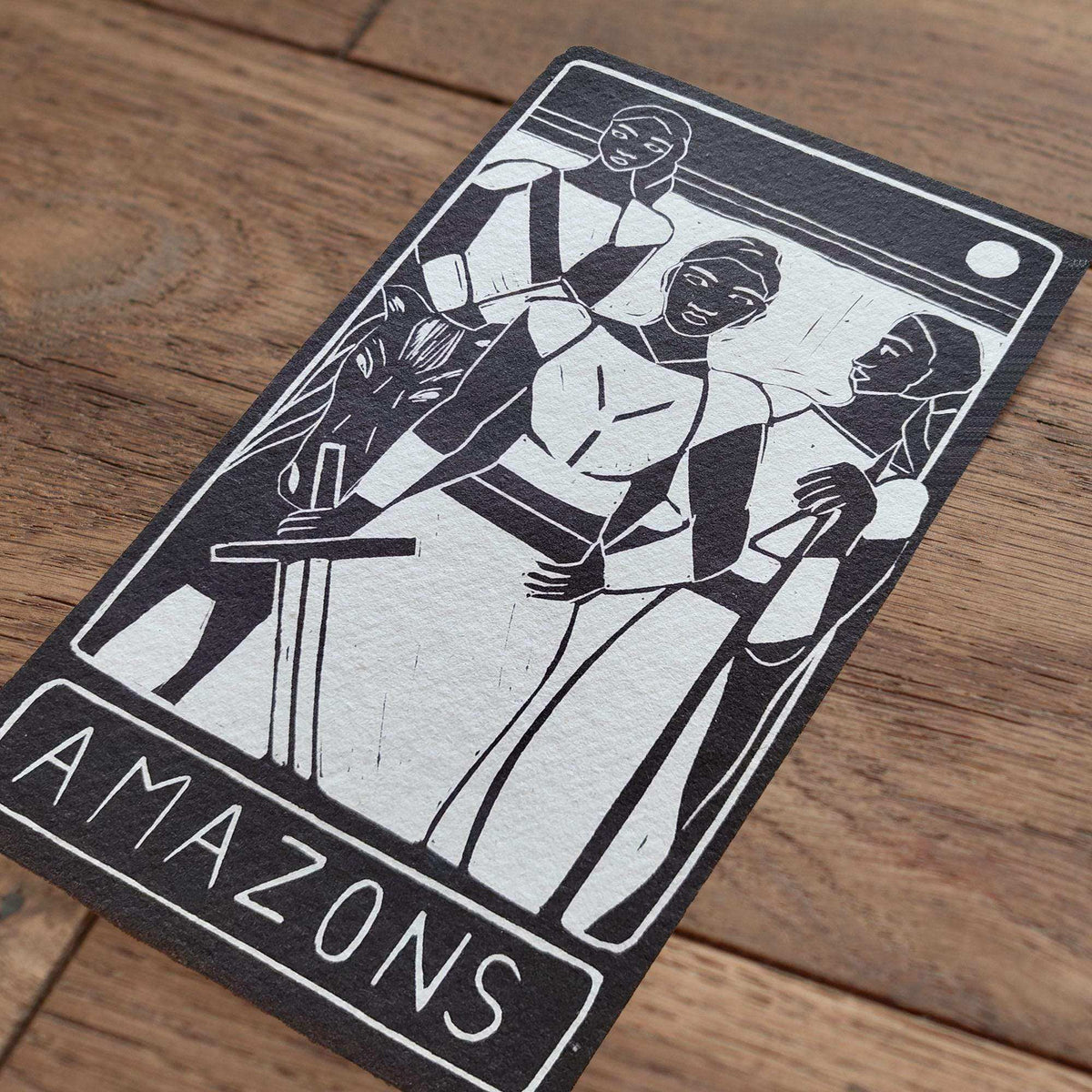 THE AMAZONS ALTAR CARD in black and white, featuring a bold linocut of three warrior women and the word Amazons