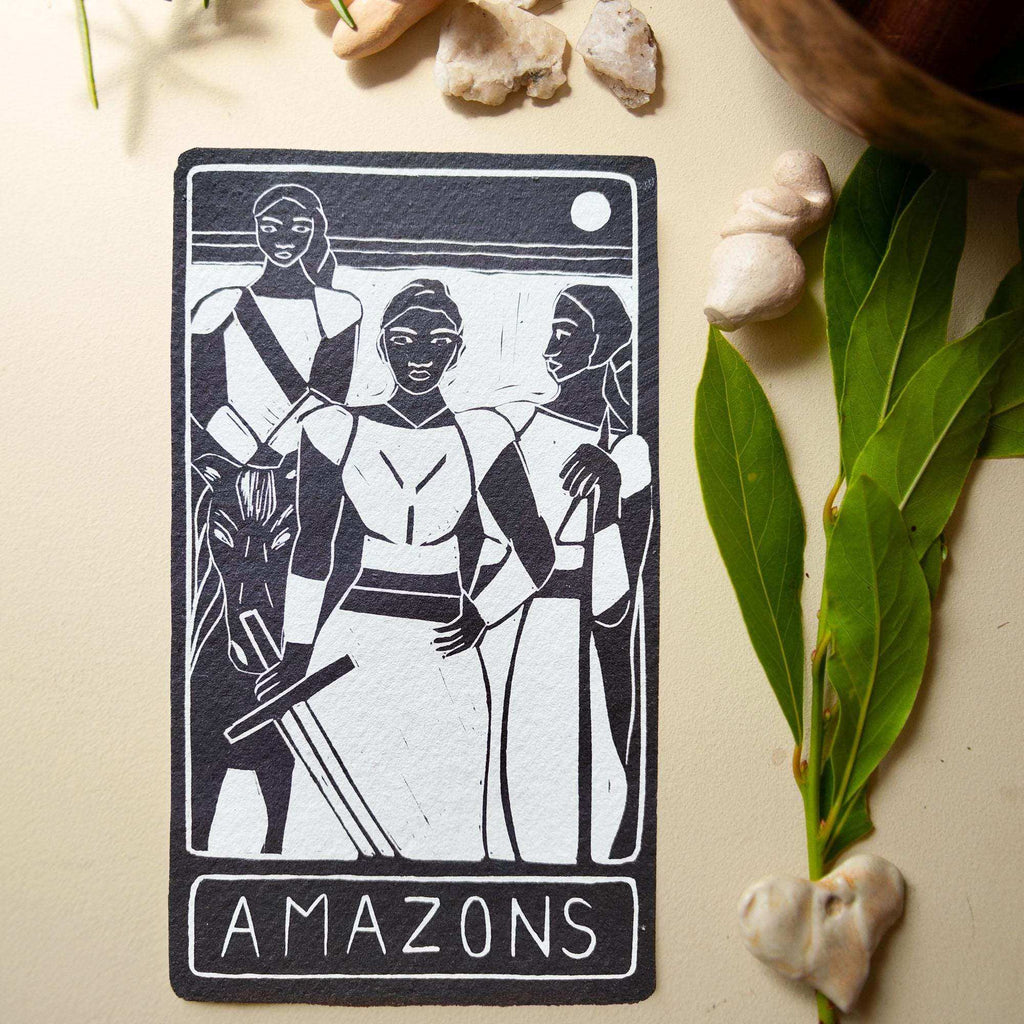 THE AMAZONS ALTAR CARD featuring a black-and-white linocut of three warrior women, with bold lettering and a moon