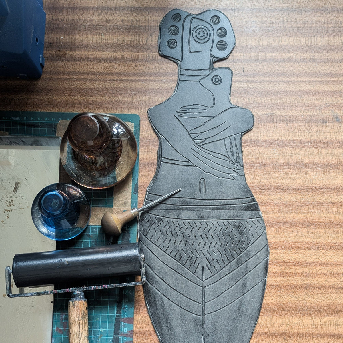 THE BIRD HEADED MOTHER linocut print showing a grey goddess figurine holding a bird-like child, with carved patterns